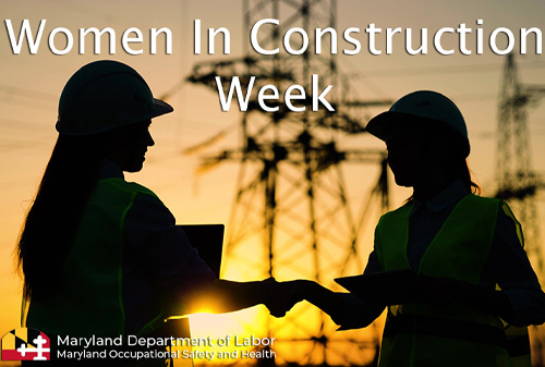 Two women in hard hats shake hands at a construction site at sunset
